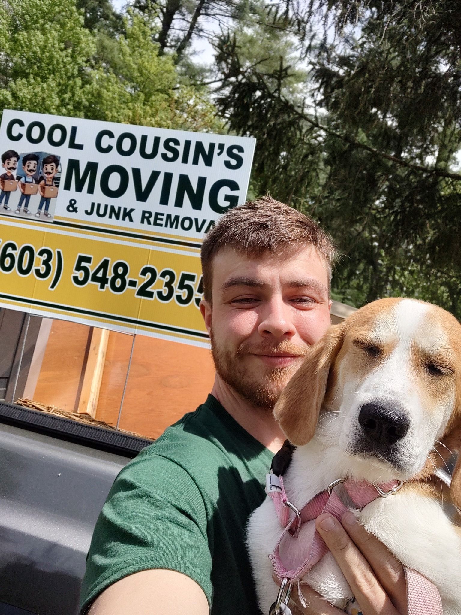 Man holding a dog in front of a moving company truck sign outdoors
