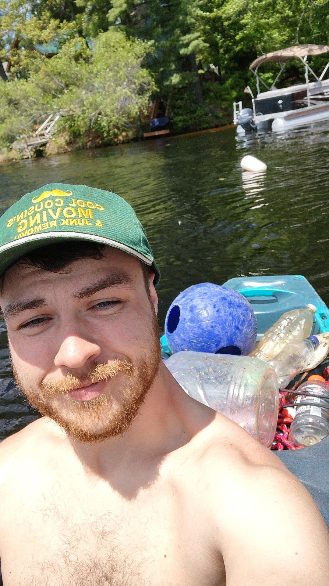 Man taking a selfie on a river in a kayak with a green cap, calm water, and trees in the background