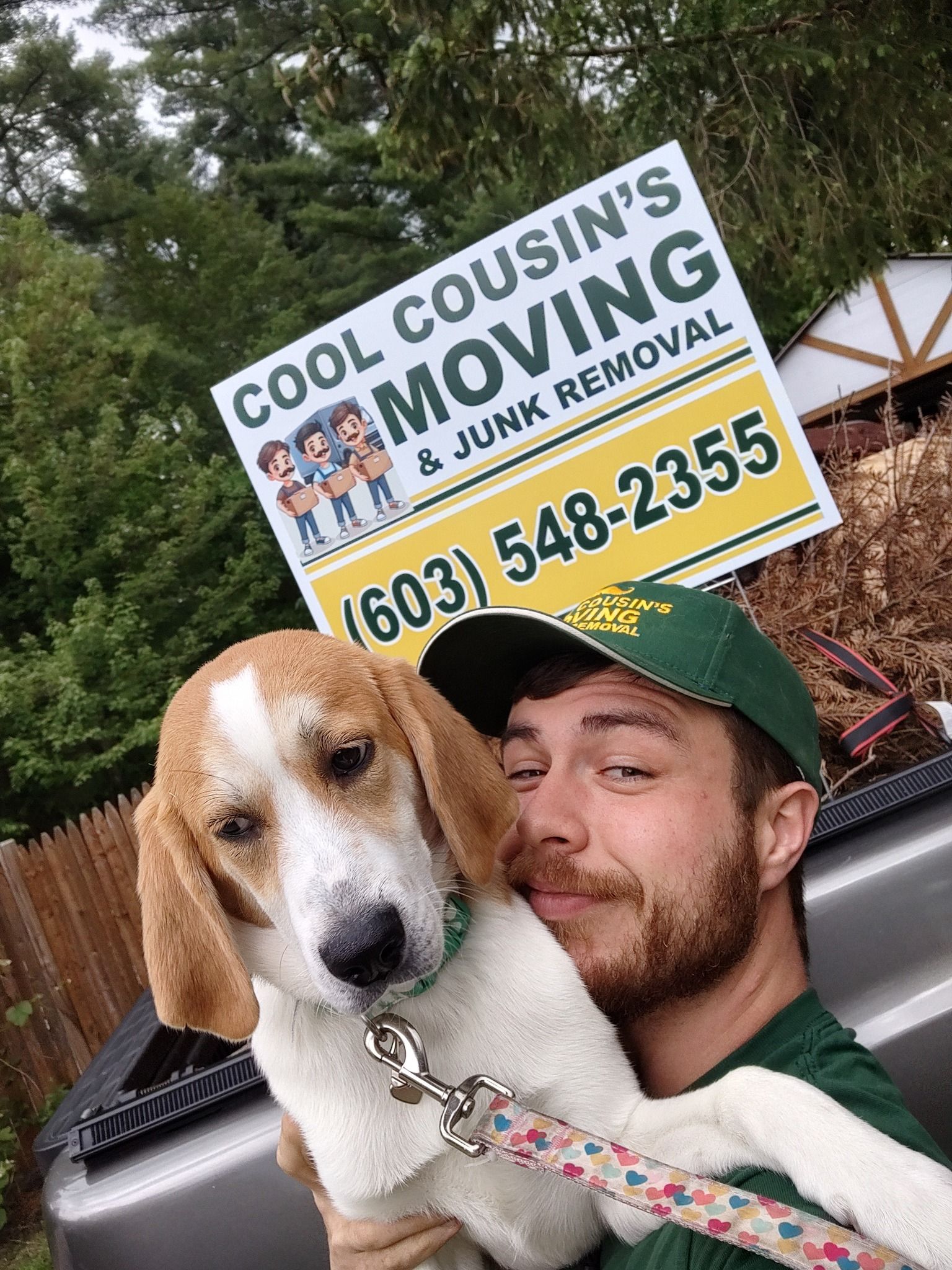 Man holding a beagle in front of a Cousin’s Moving sign and truck bed