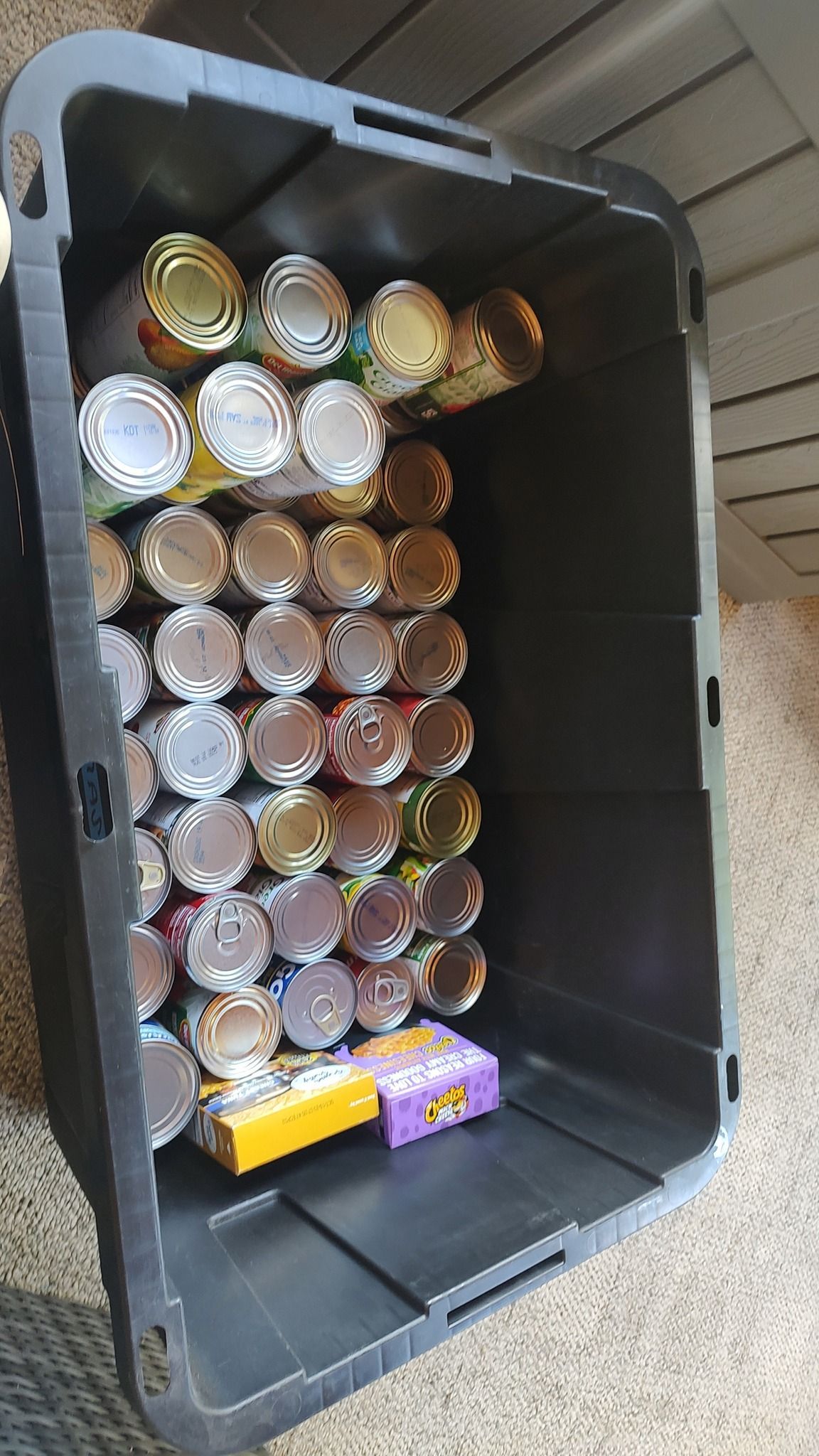 Black storage bin filled with stacked canned drinks and two snack bars at the bottom
