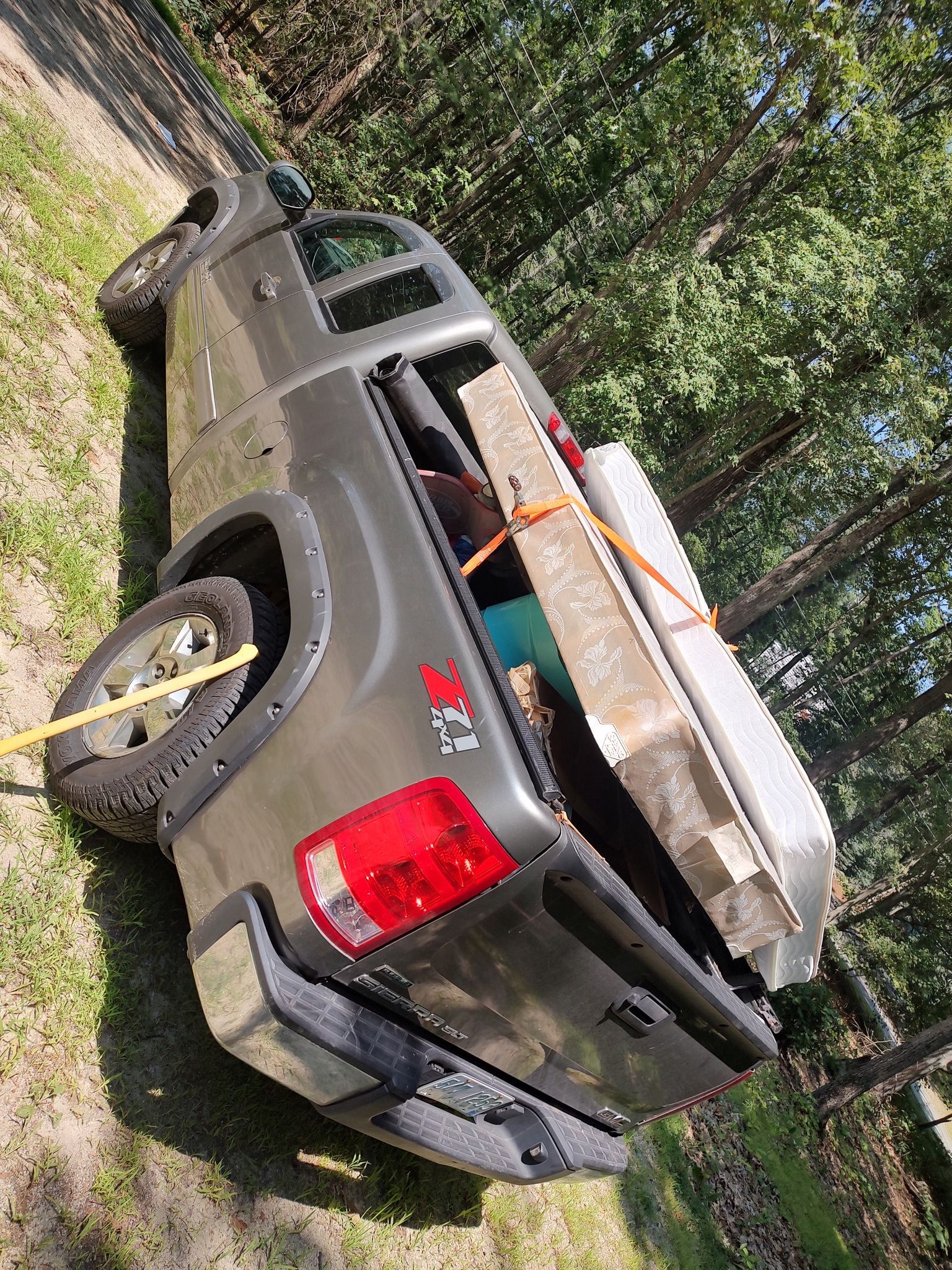 Gray pickup truck parked on grass, carrying lumber and a white kayak in the bed.