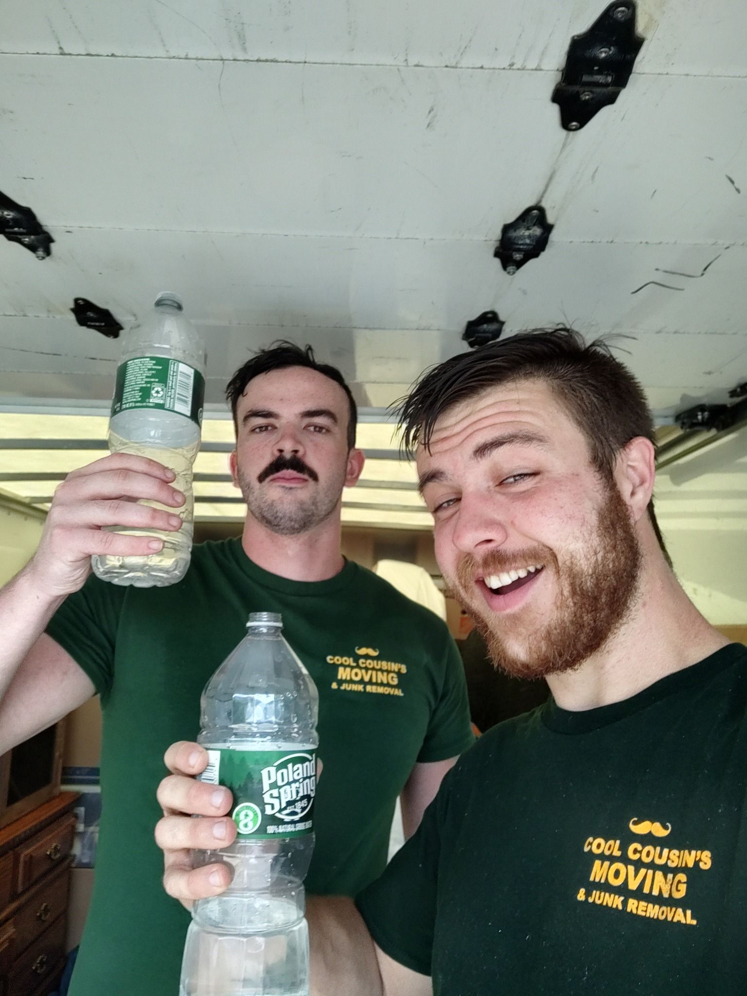 Two smiling people holding bottles in a bright indoor setting with a cracked ceiling.