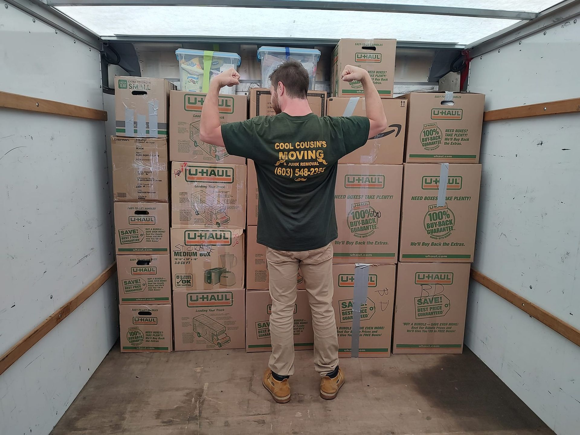 Person inside a moving truck stacks cardboard boxes and holds up a box overhead.