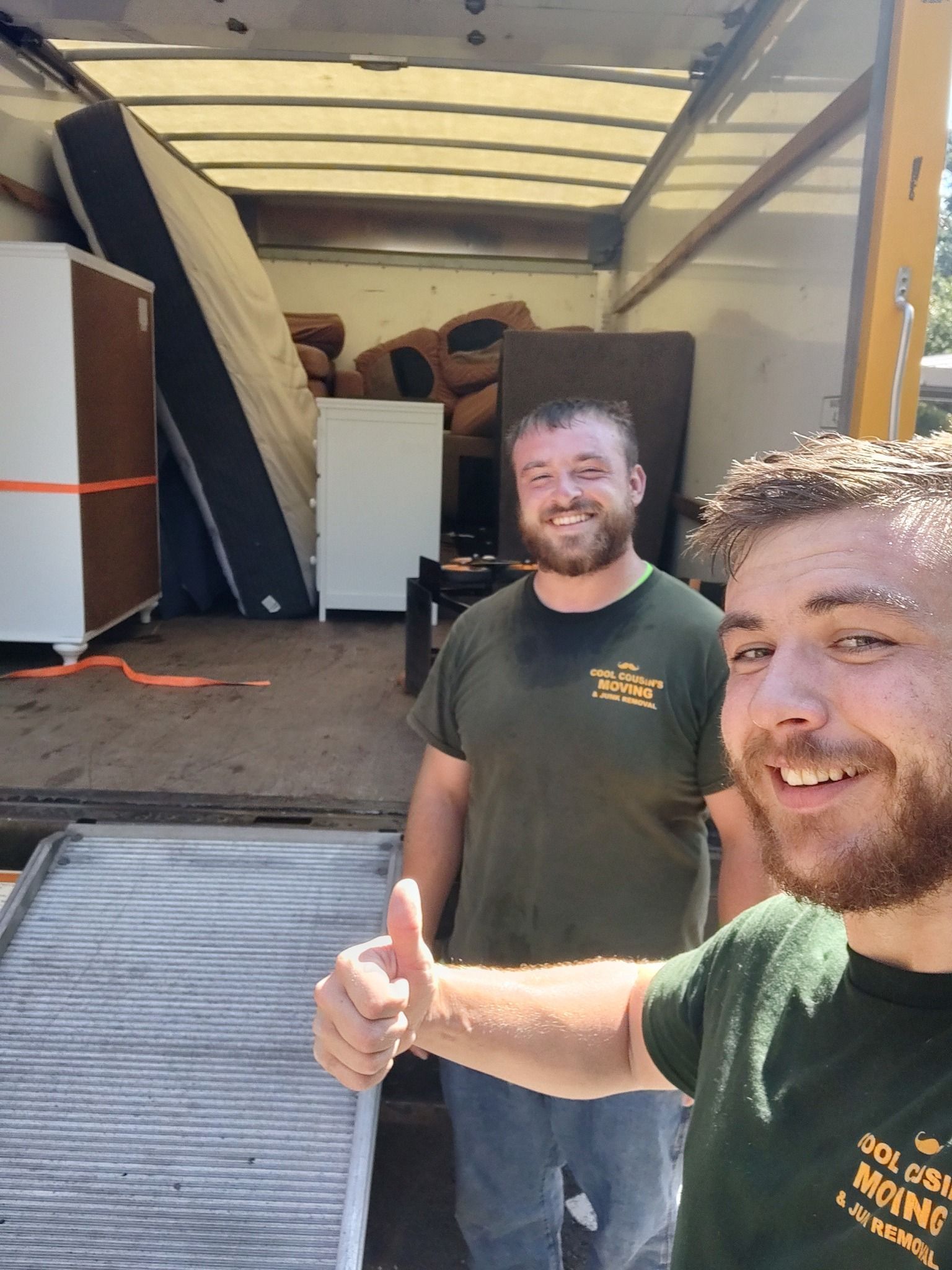 Two smiling men beside a moving truck, one giving a thumbs-up in the foreground.