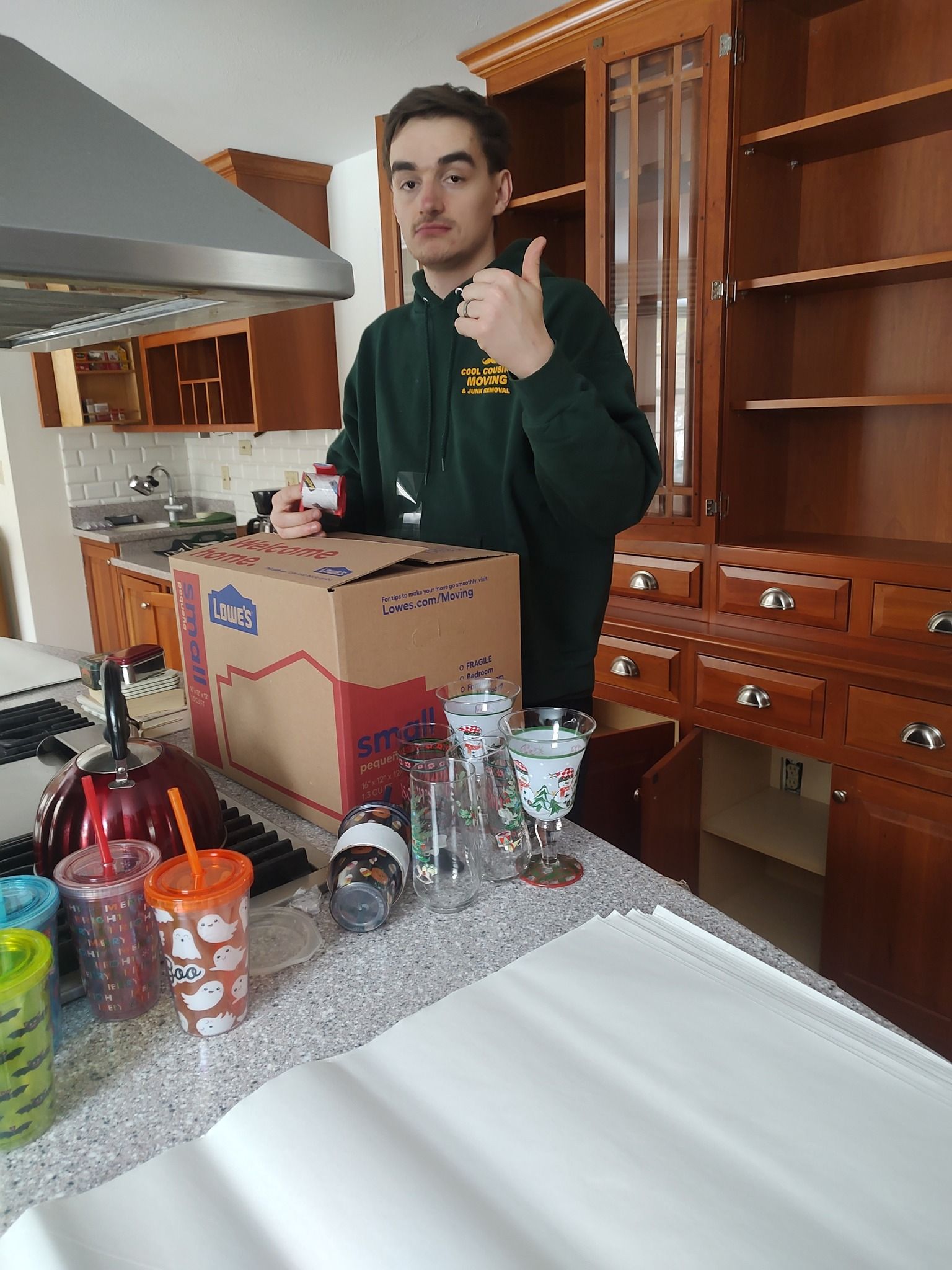 Person in a kitchen giving a thumbs-up beside a table with groceries and cardboard boxes.