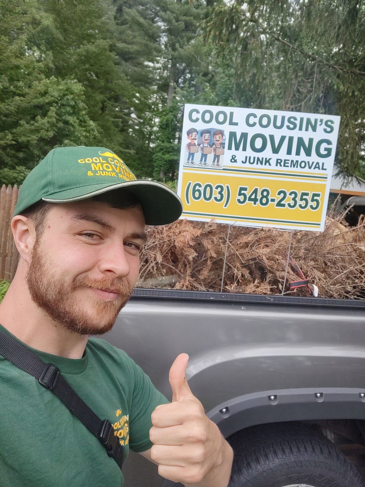 Man giving a thumbs-up beside a COOL COUSIN'S MOVING truck sign in a wooded area