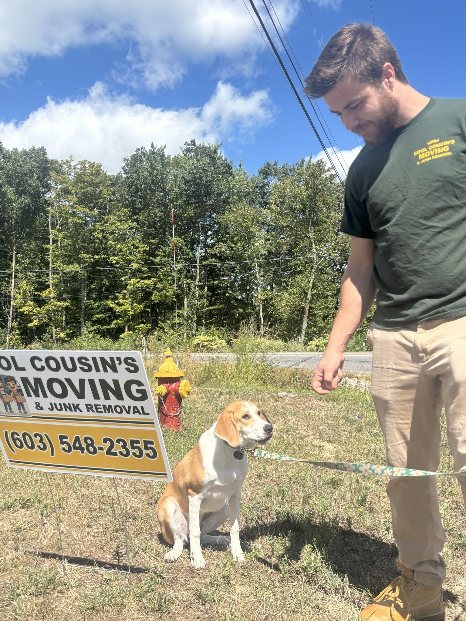 Man with a beagle beside a landscaping sign in a grassy yard under a blue sky