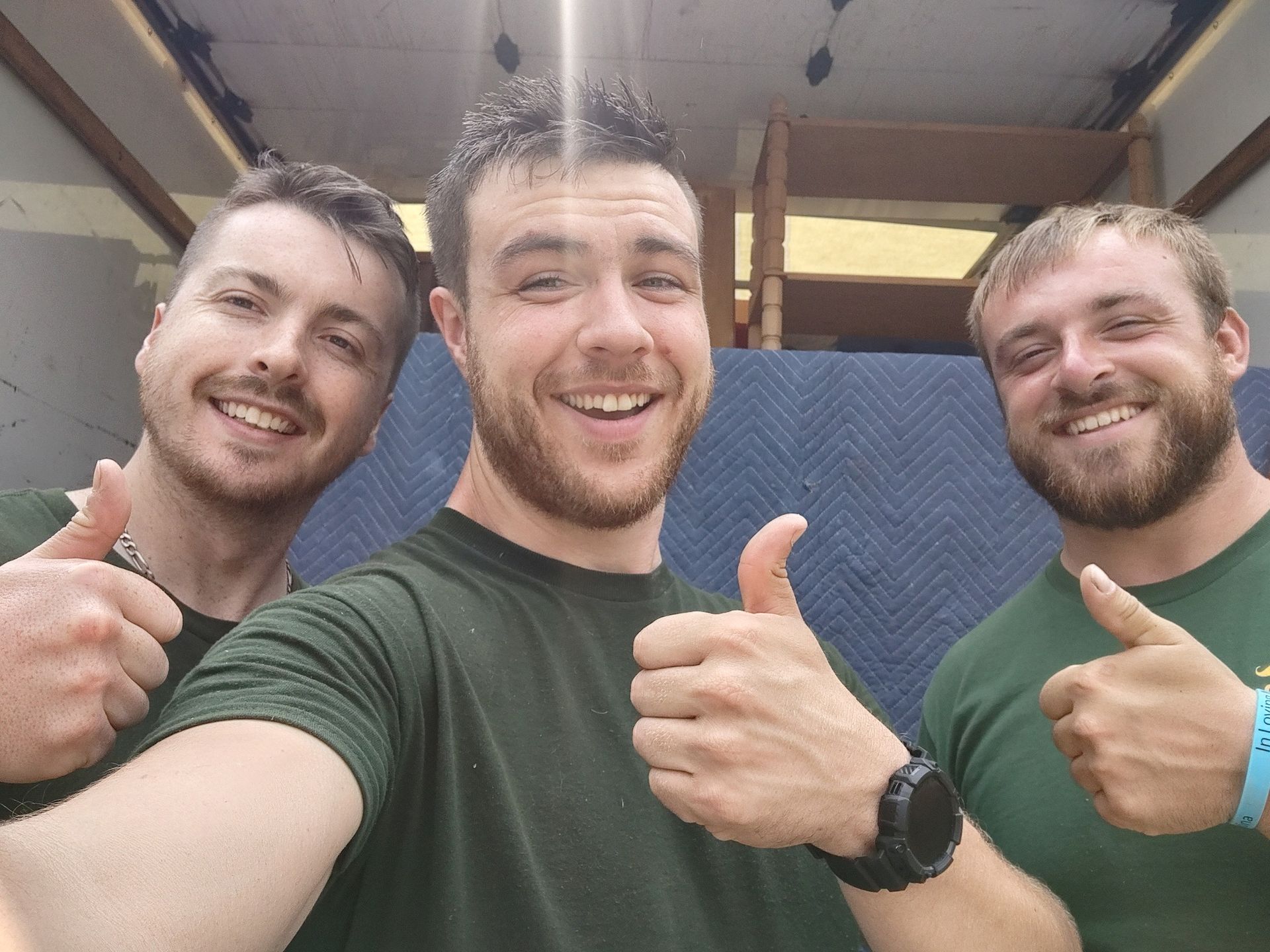 Three smiling people in a room, posing with thumbs up in front of a blue wall.