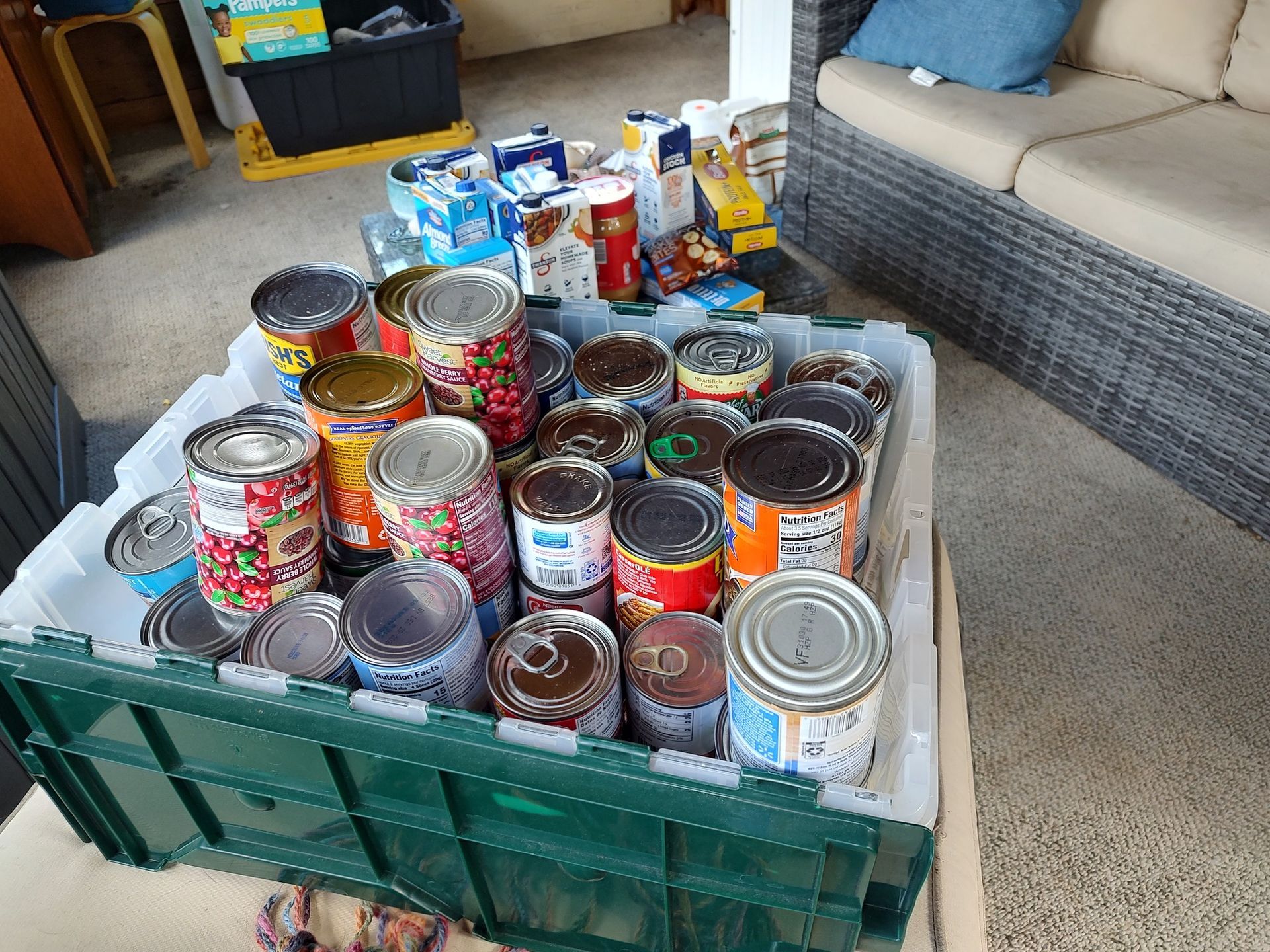 Assorted canned goods and food items packed in a green crate in a living room