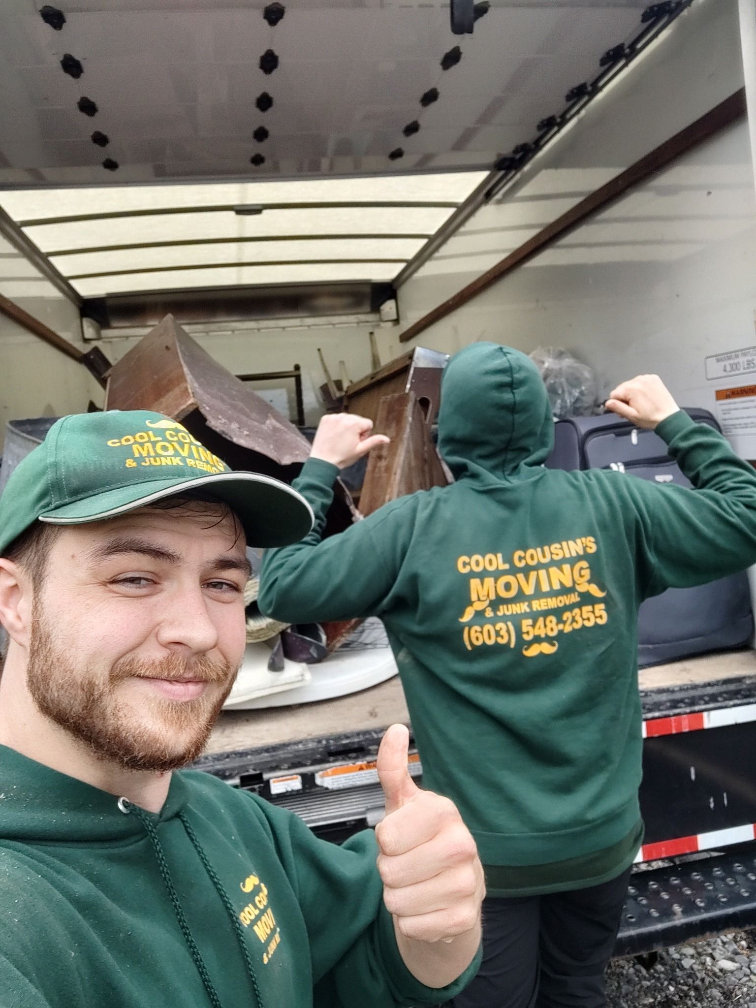 Two movers in green hoodies loading a truck; one gives a thumbs-up in the foreground.