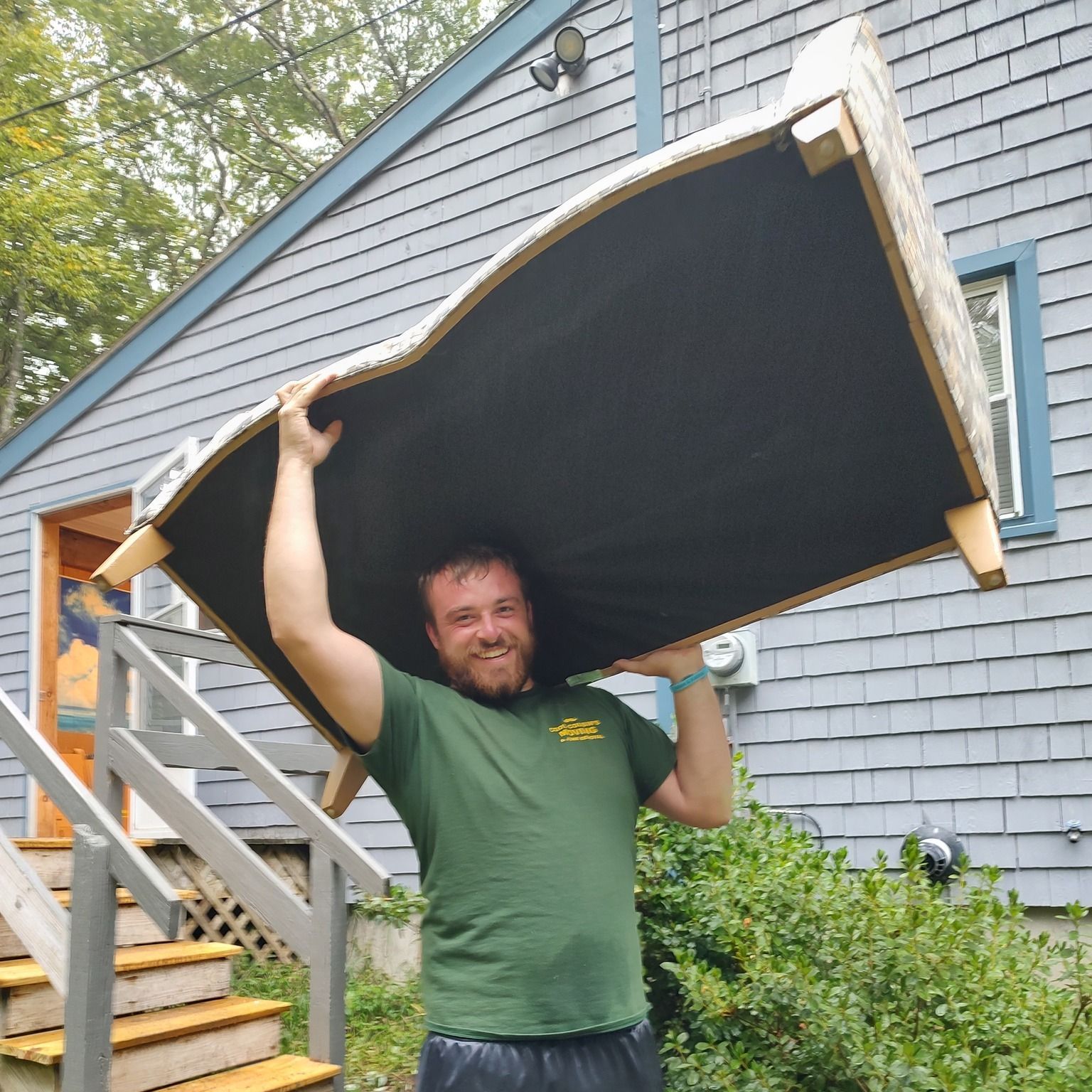 Man holding a large black panel outside a blue house, standing by outdoor stairs.