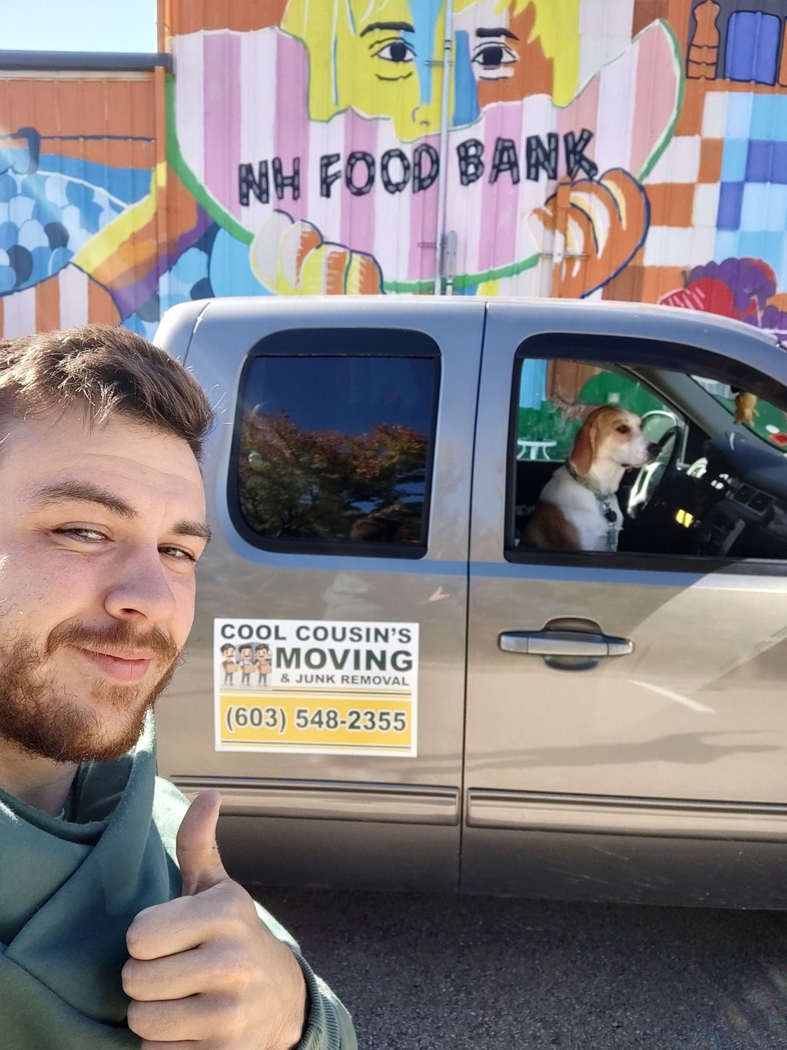 Selfie beside a moving van at a food bank mural, with a dog in the truck window.