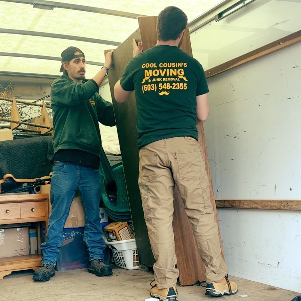 Two movers loading a tall piece of furniture into a truck trailer