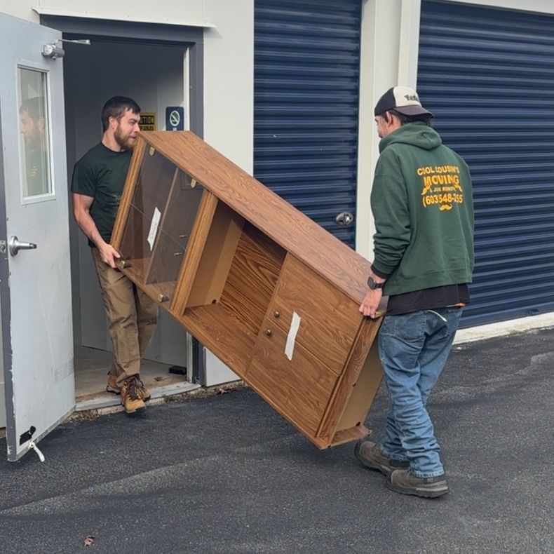 Two workers carry a large wooden cabinet outside a building near a doorway.