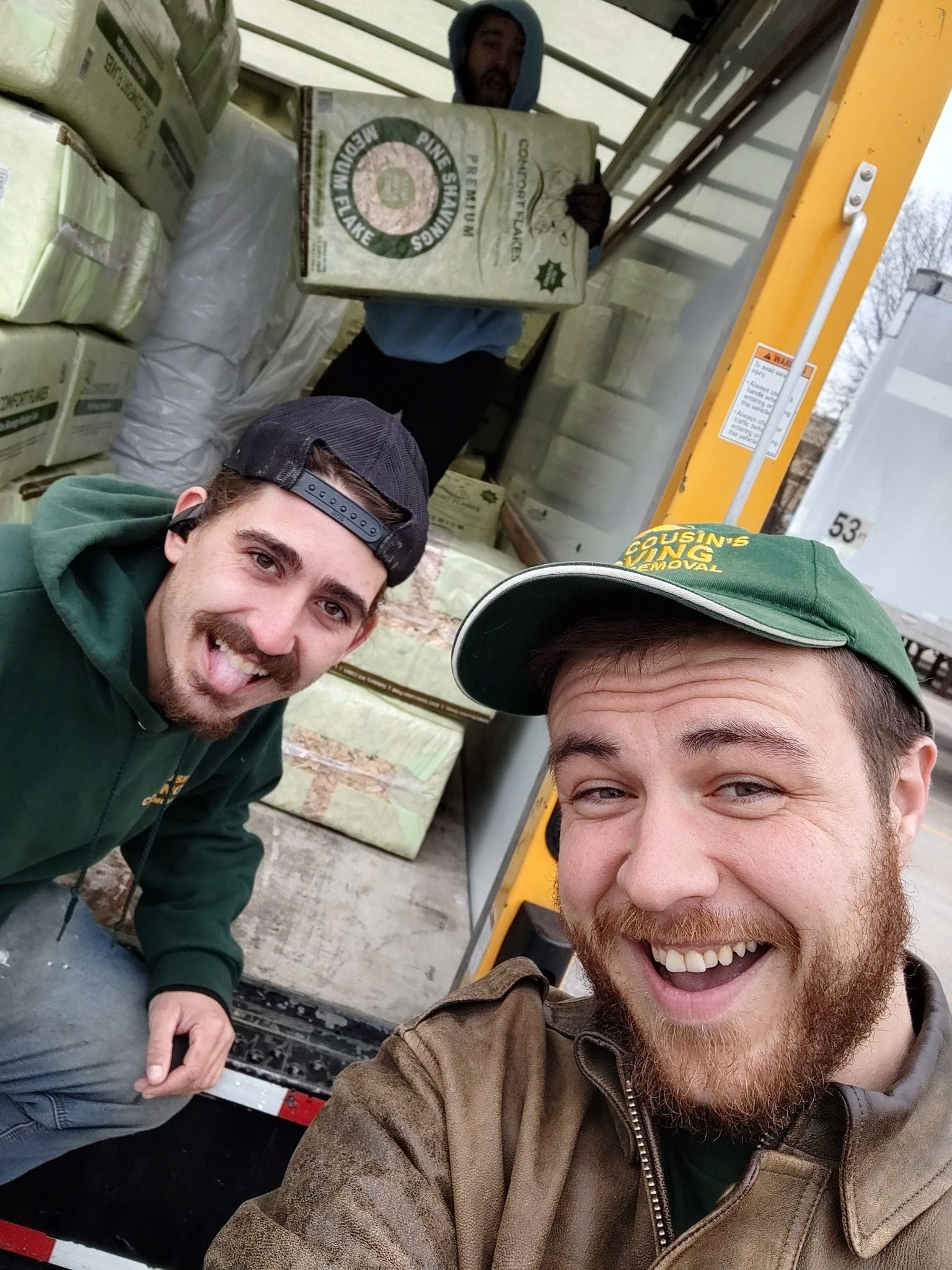 Three smiling workers posing in a truck loading area with boxes around them.
