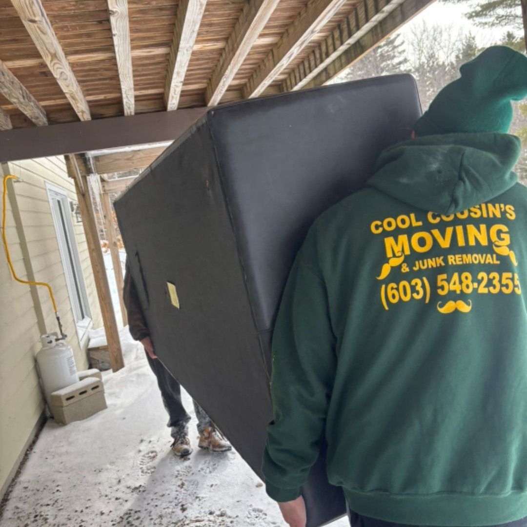 Movers carrying a large black couch down a snowy apartment walkway under a covered porch