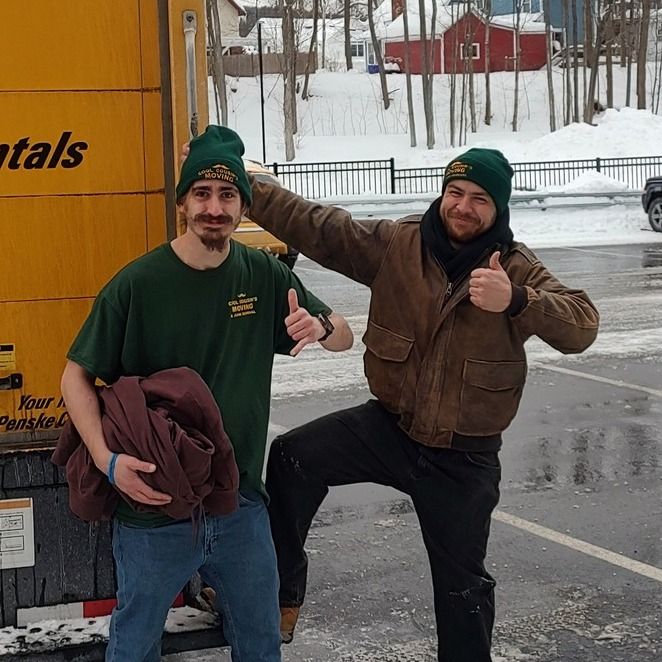 Two people posing outdoors in snow, smiling and giving thumbs up beside a yellow truck