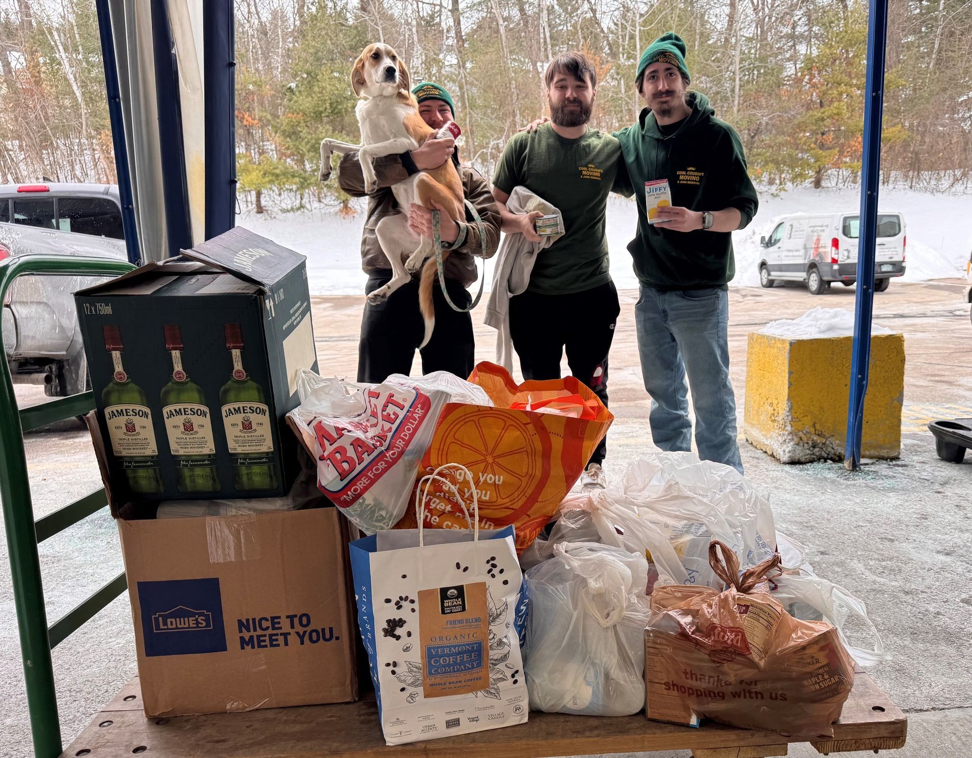 People posing with a dog beside a table of food donations in a snowy outdoor setting