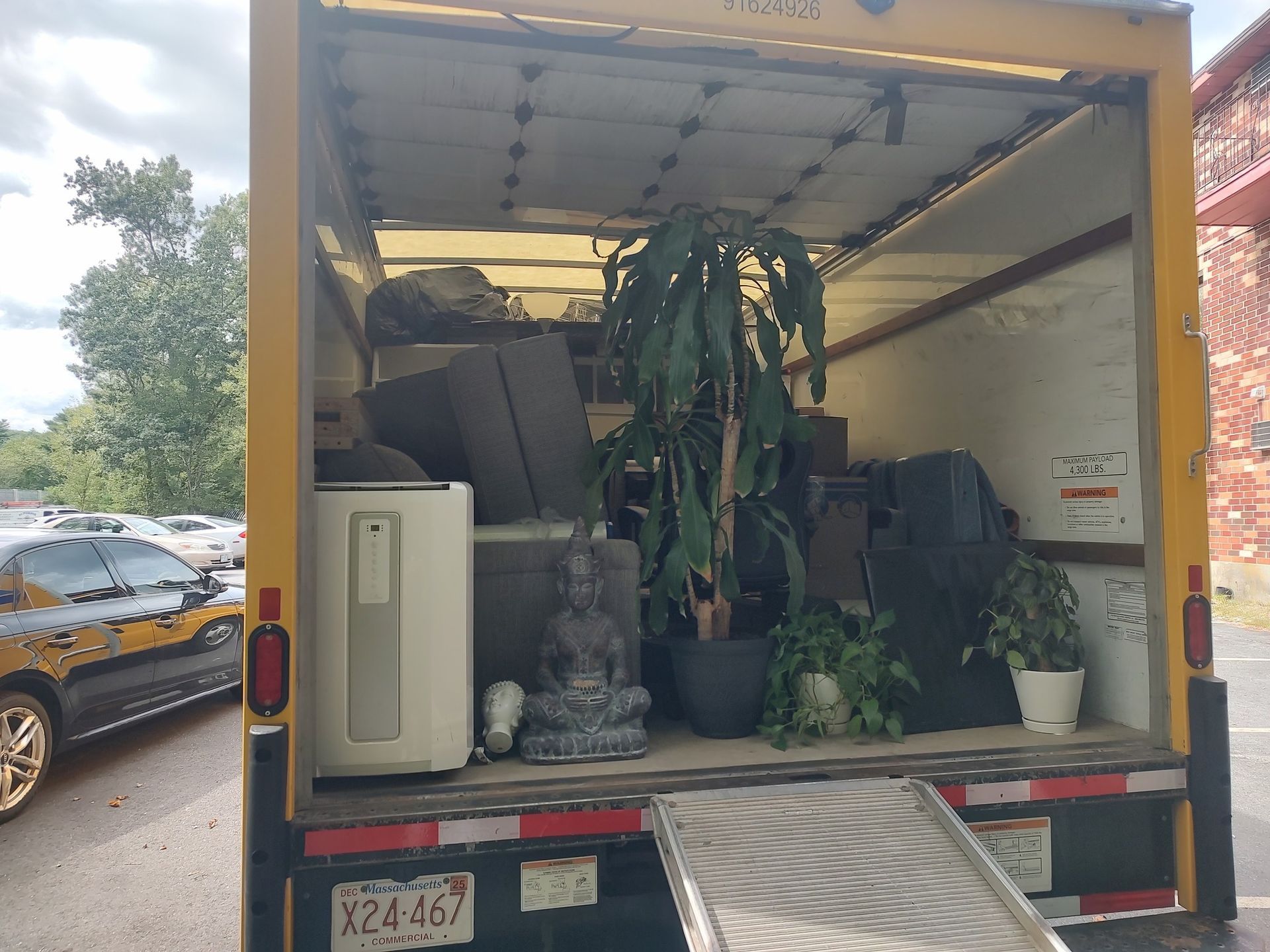 Open moving truck packed with furniture, plants, and household items on a street.