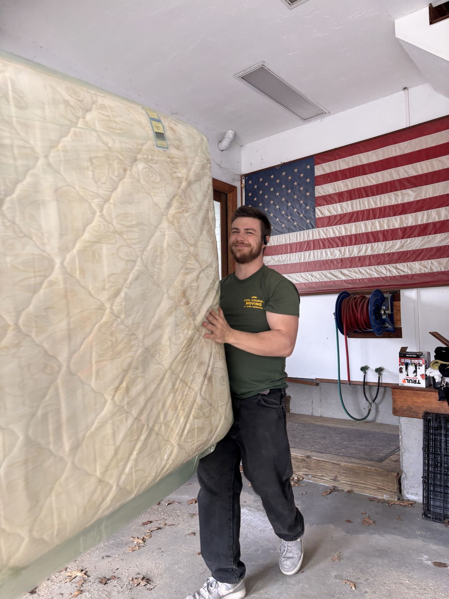 Person carrying a mattress in a garage with an American flag on the wall.
