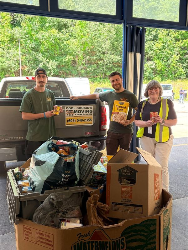 Three volunteers in green shirts stand behind a cart loaded with bags of donations.