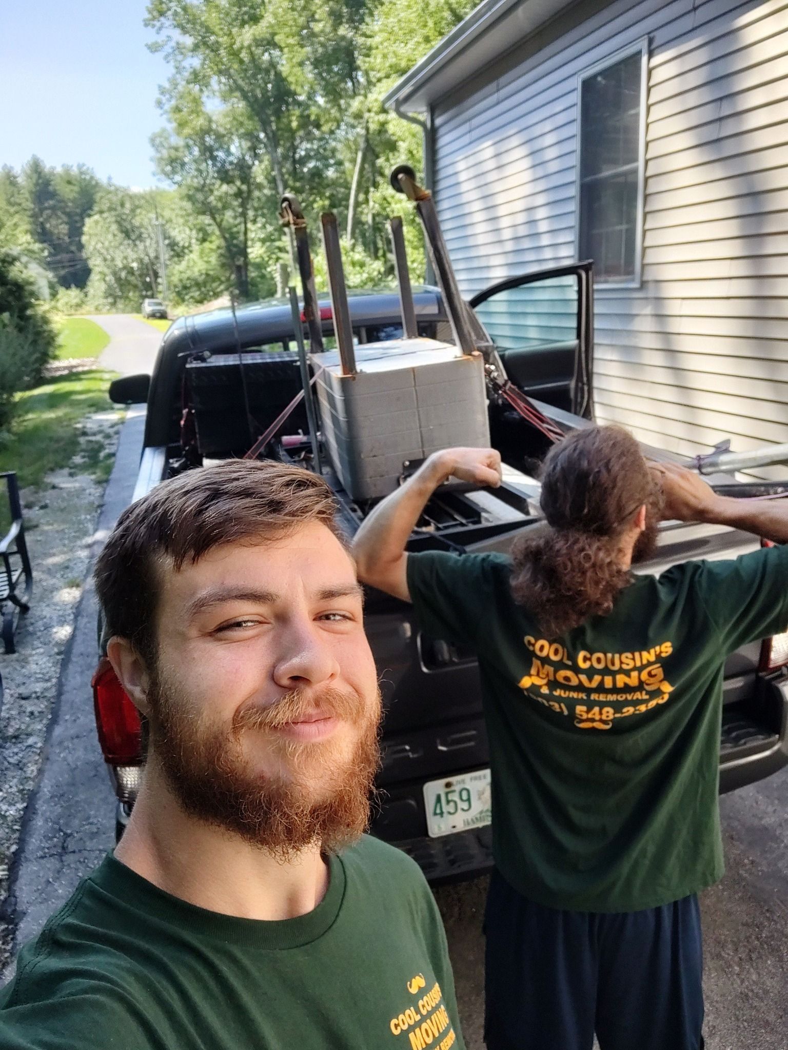 Two people loading furniture into a pickup truck beside a house on a sunny day