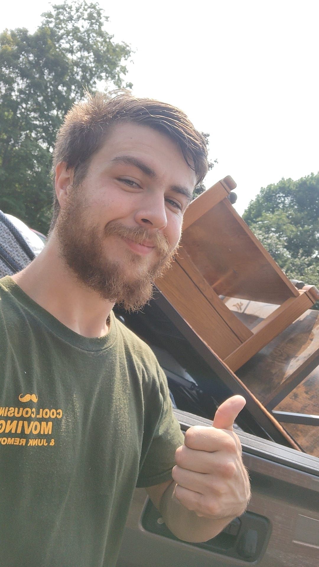 Man smiling and giving thumbs-up beside a car carrying a wooden chair outdoors