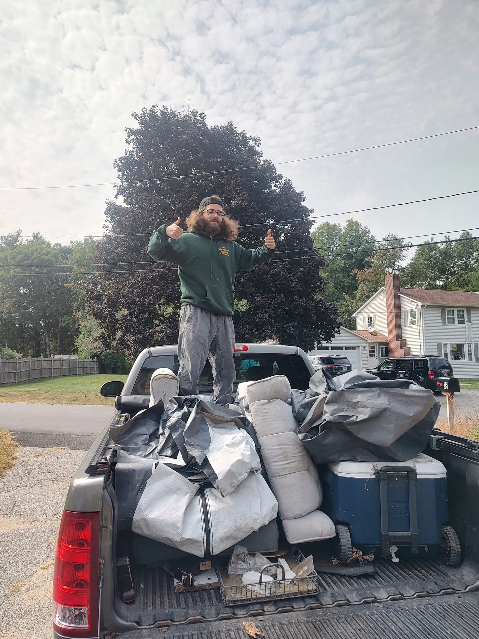 Person standing on a truck bed loaded with trash bags and containers, outdoors in a driveway
