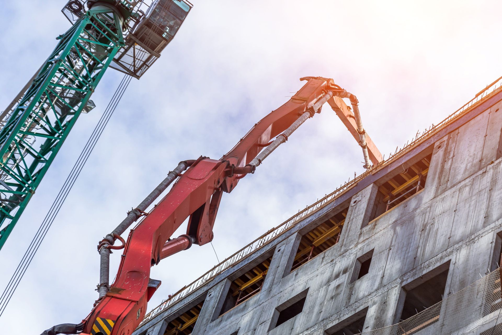 Construction cranes working on a building under construction, viewed from below against a bright sky