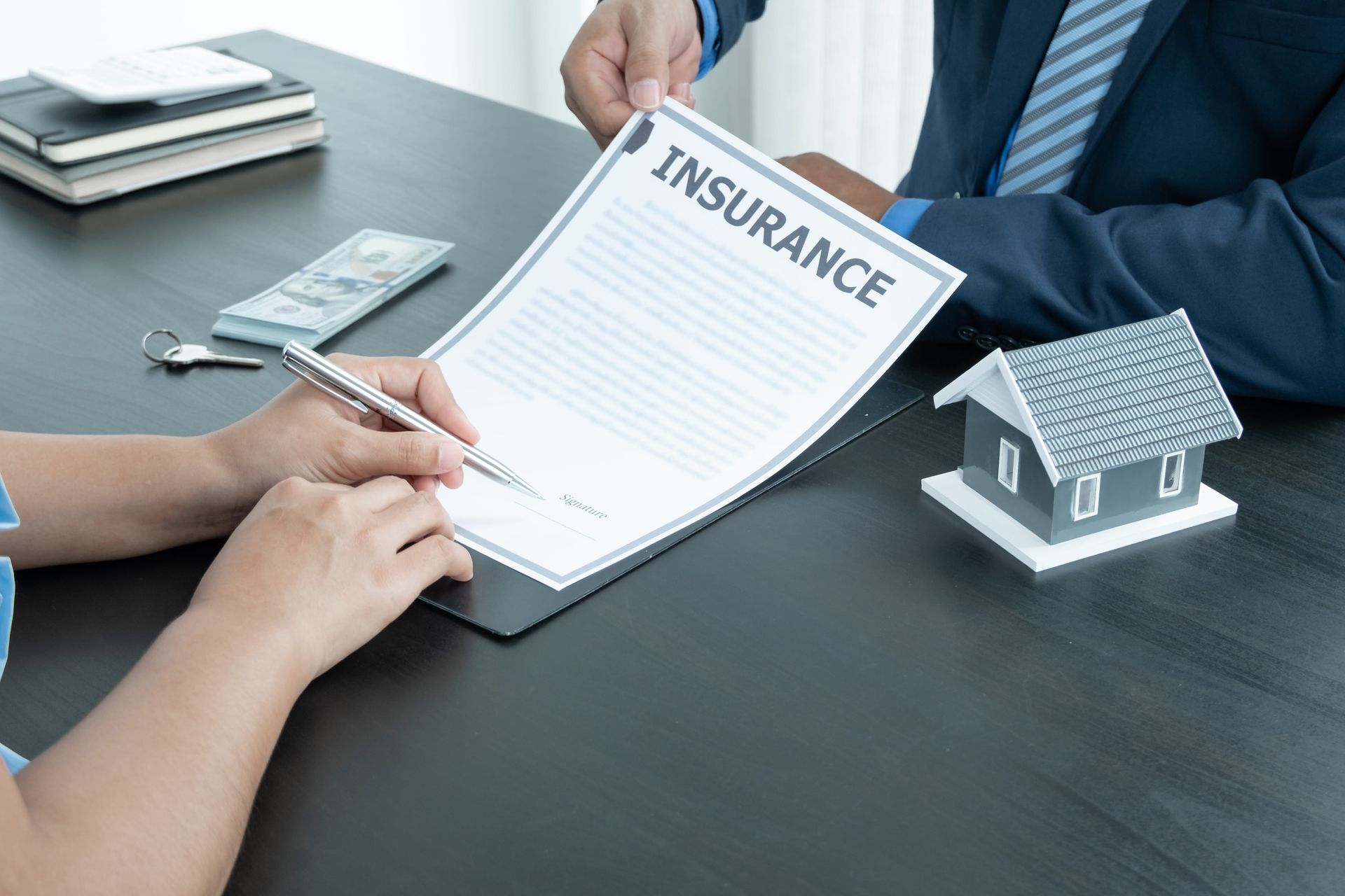 Hands signing an insurance form beside a small house model on a desk