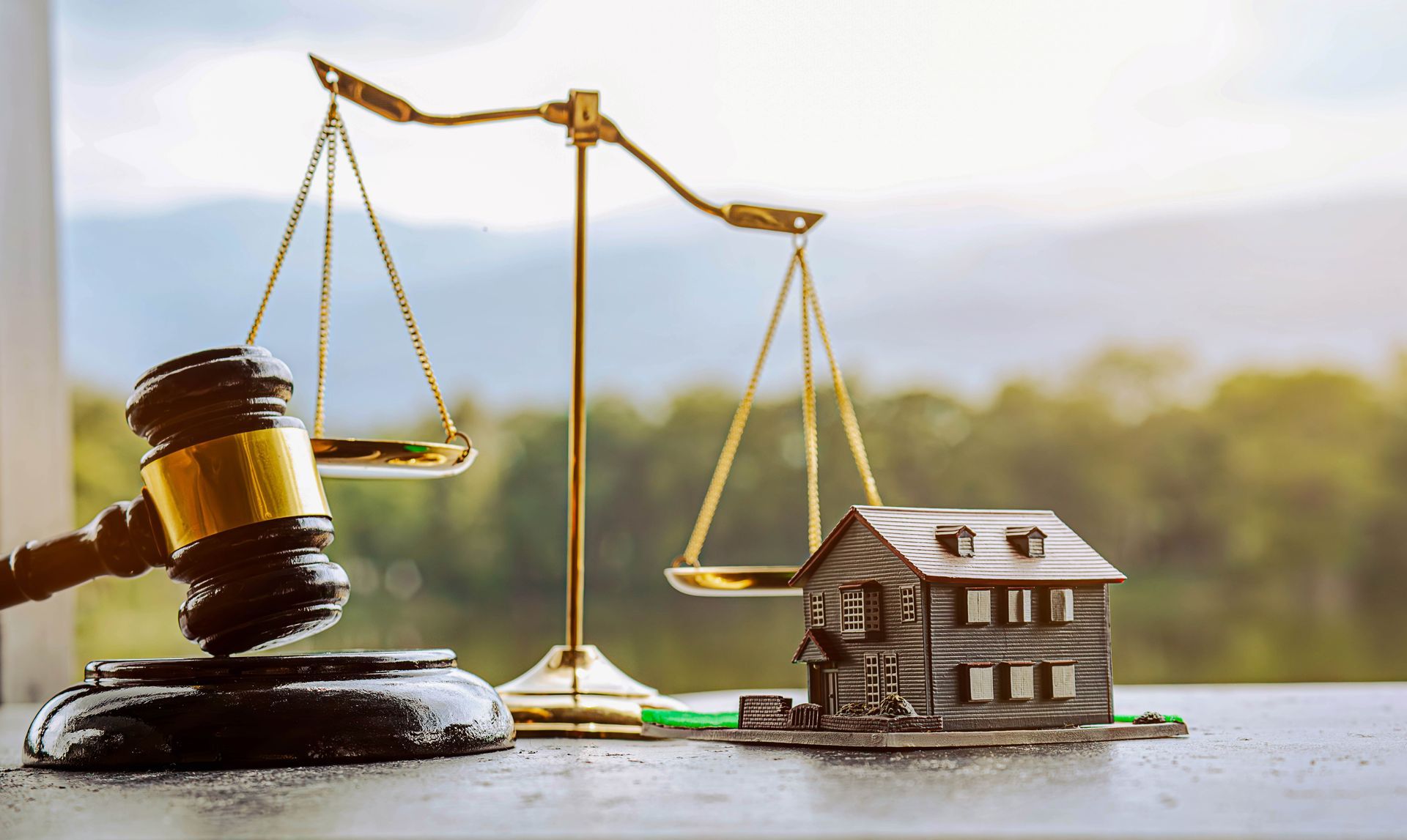 Gavel and balance scales next to a miniature house, symbolizing real estate law with natural background.