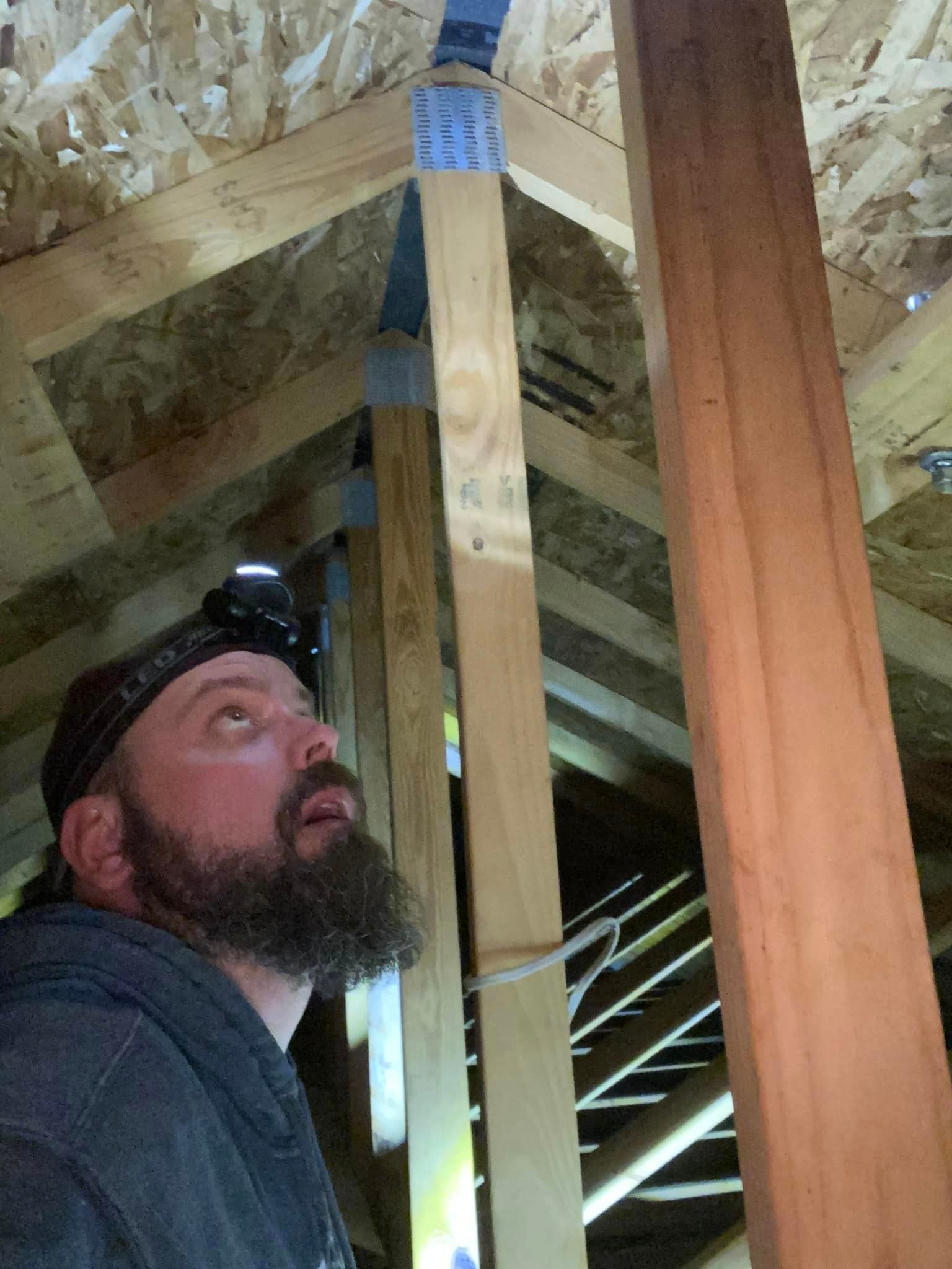 Man in a hard hat inspecting attic framing and roof trusses overhead
