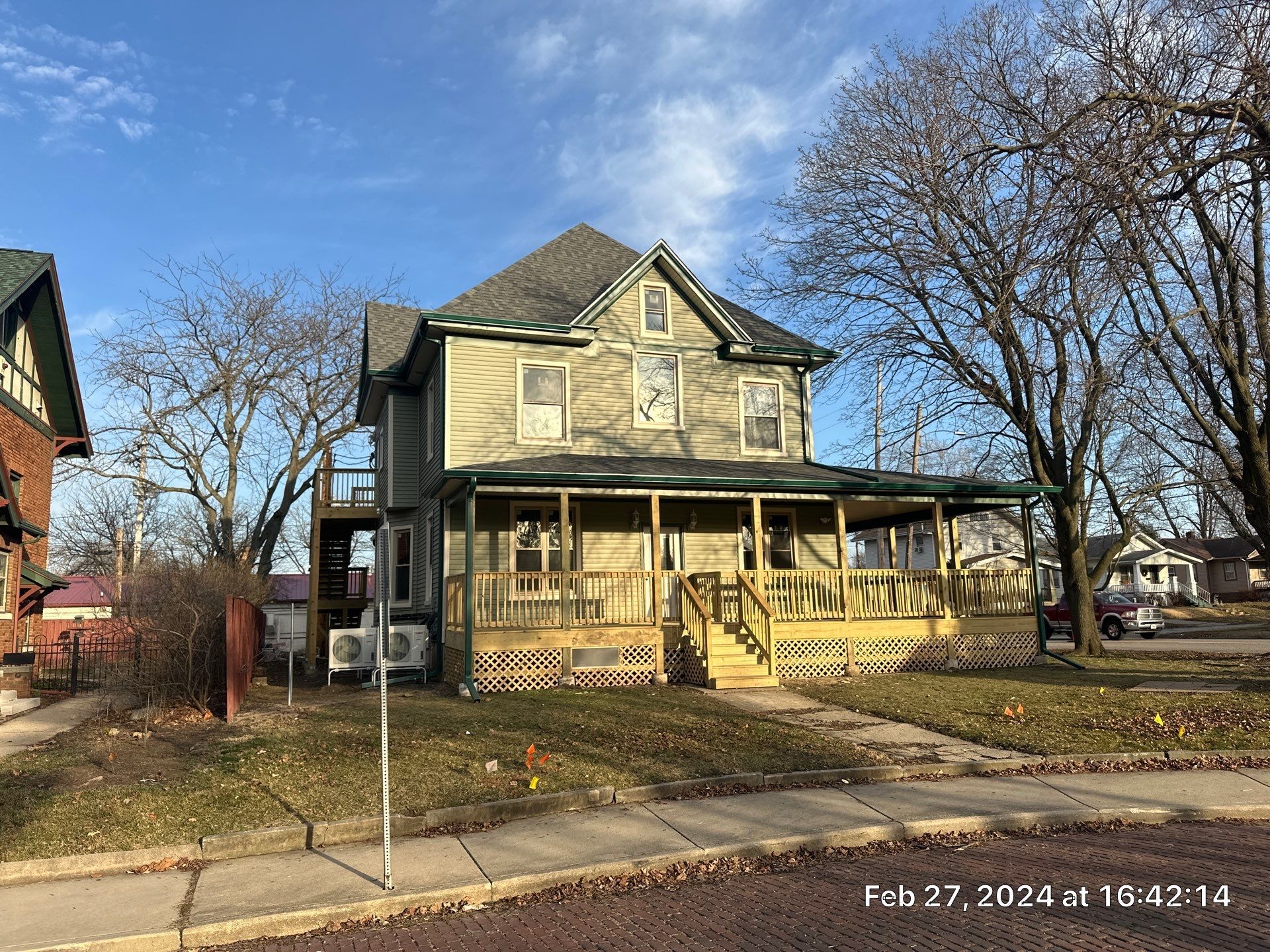 Two-story beige house with a front porch and bare trees on a sunny day