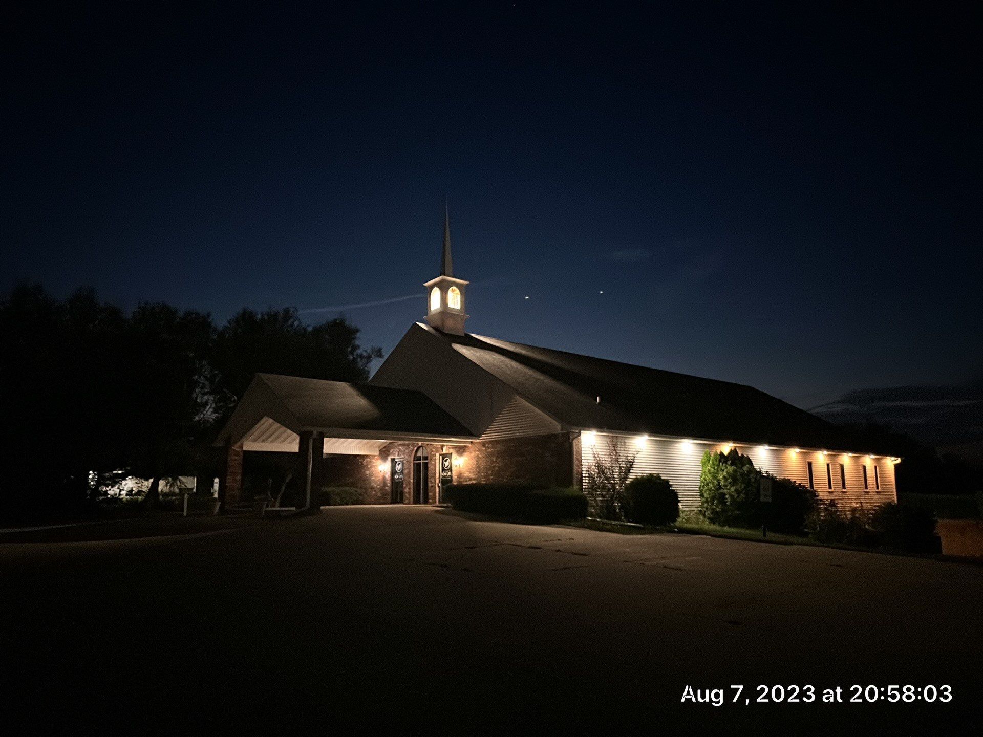 Nighttime view of a lit church building with a steeple against a dark sky