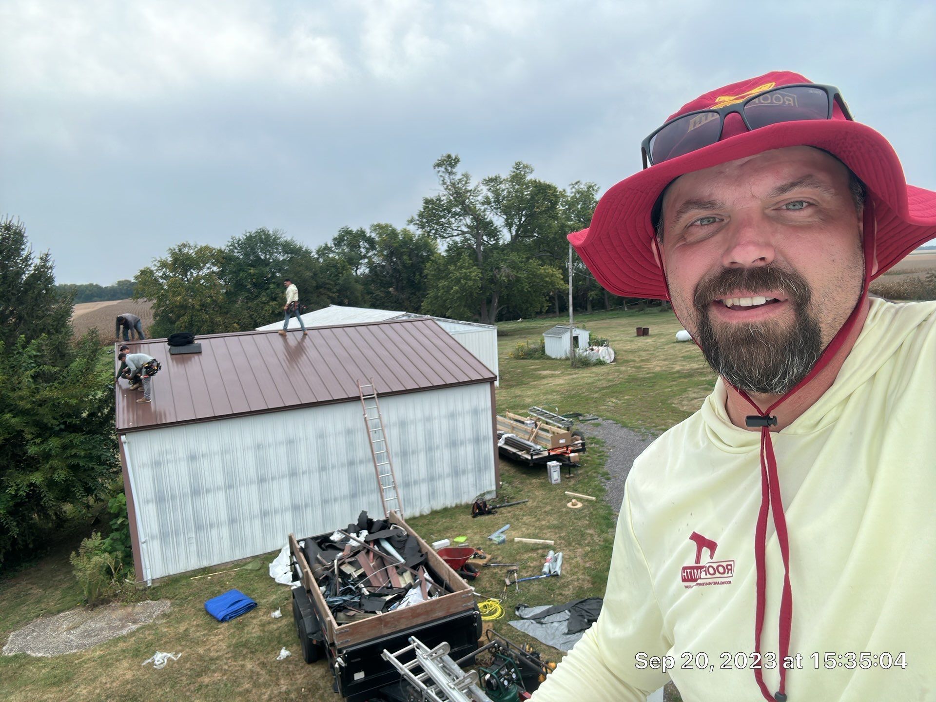 Man in red hat smiling beside a shed roof and scattered debris in a yard