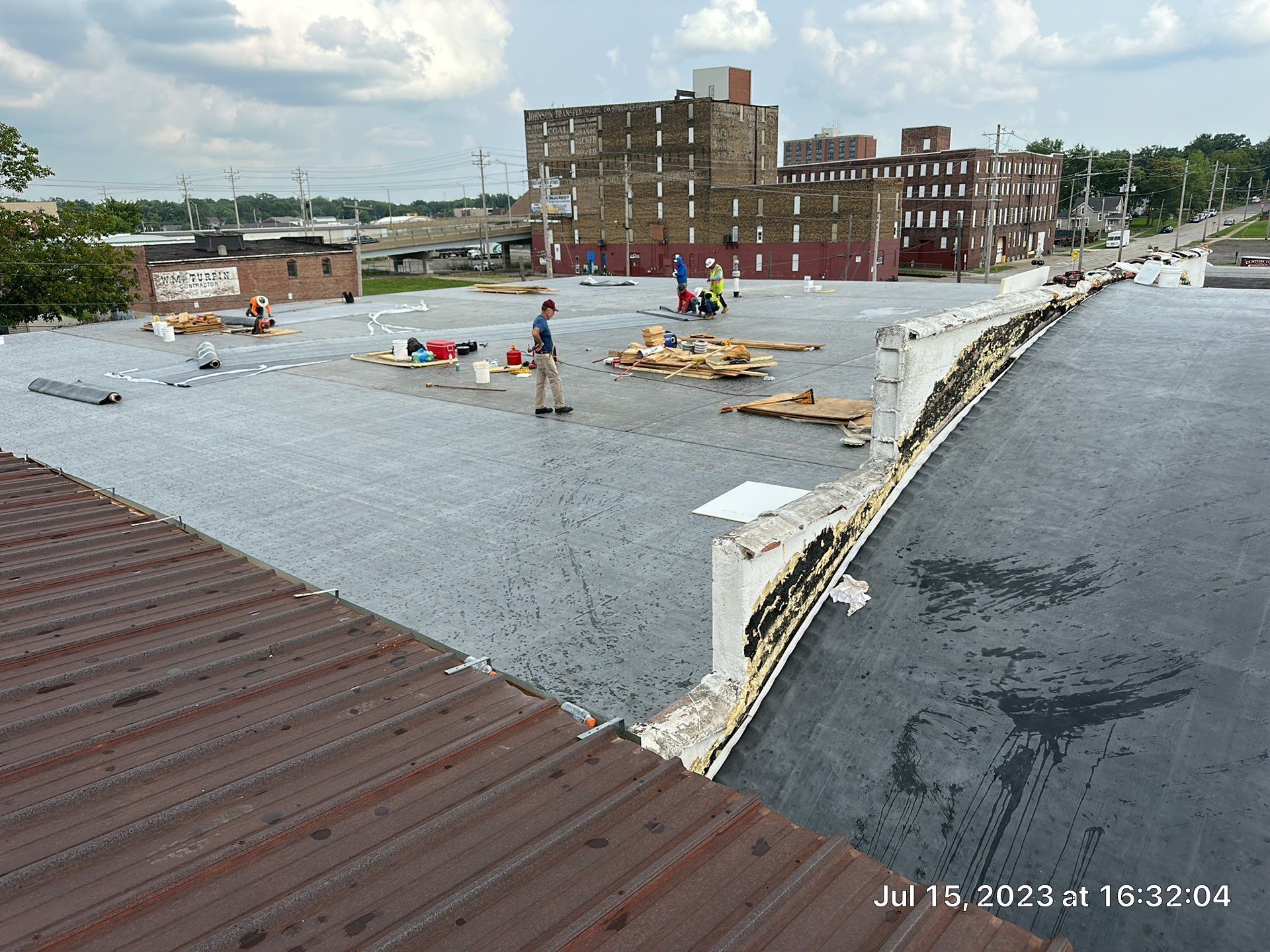 Rooftop with standing water and debris after storm damage, with damaged buildings in the background
