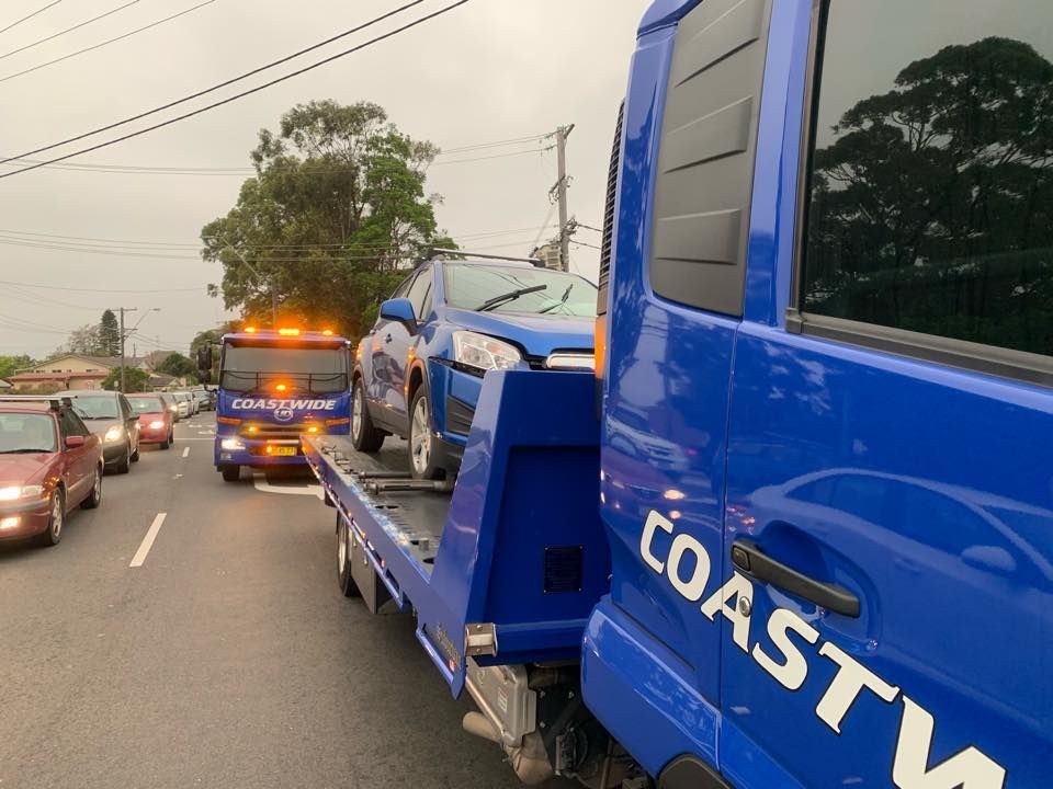 A blue tow truck is towing away a car that was broken down on the side of the road — Coastwide Towing & Transport In Berkeley Vale, NSW