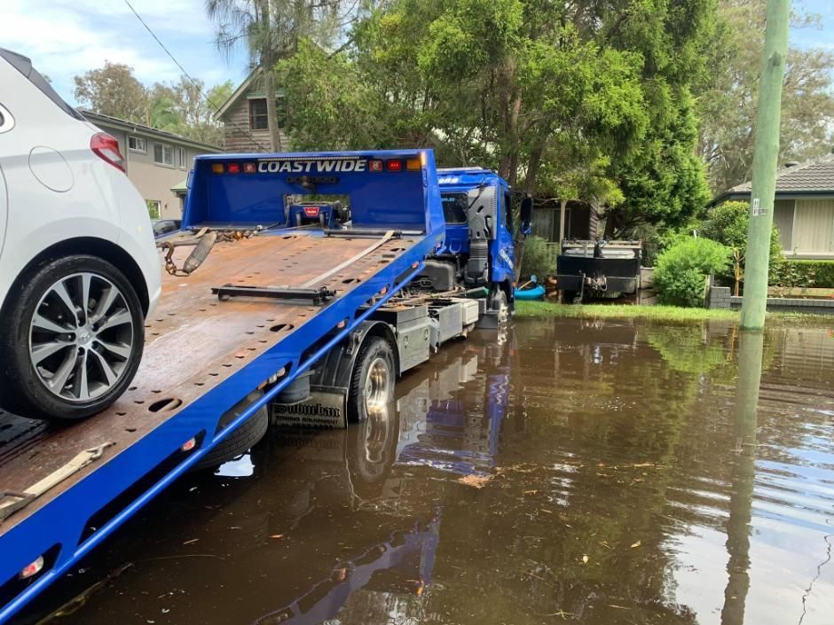 A tow truck is towing a car in a flooded street — Coastwide Towing & Transport In Berkeley Vale, NSW