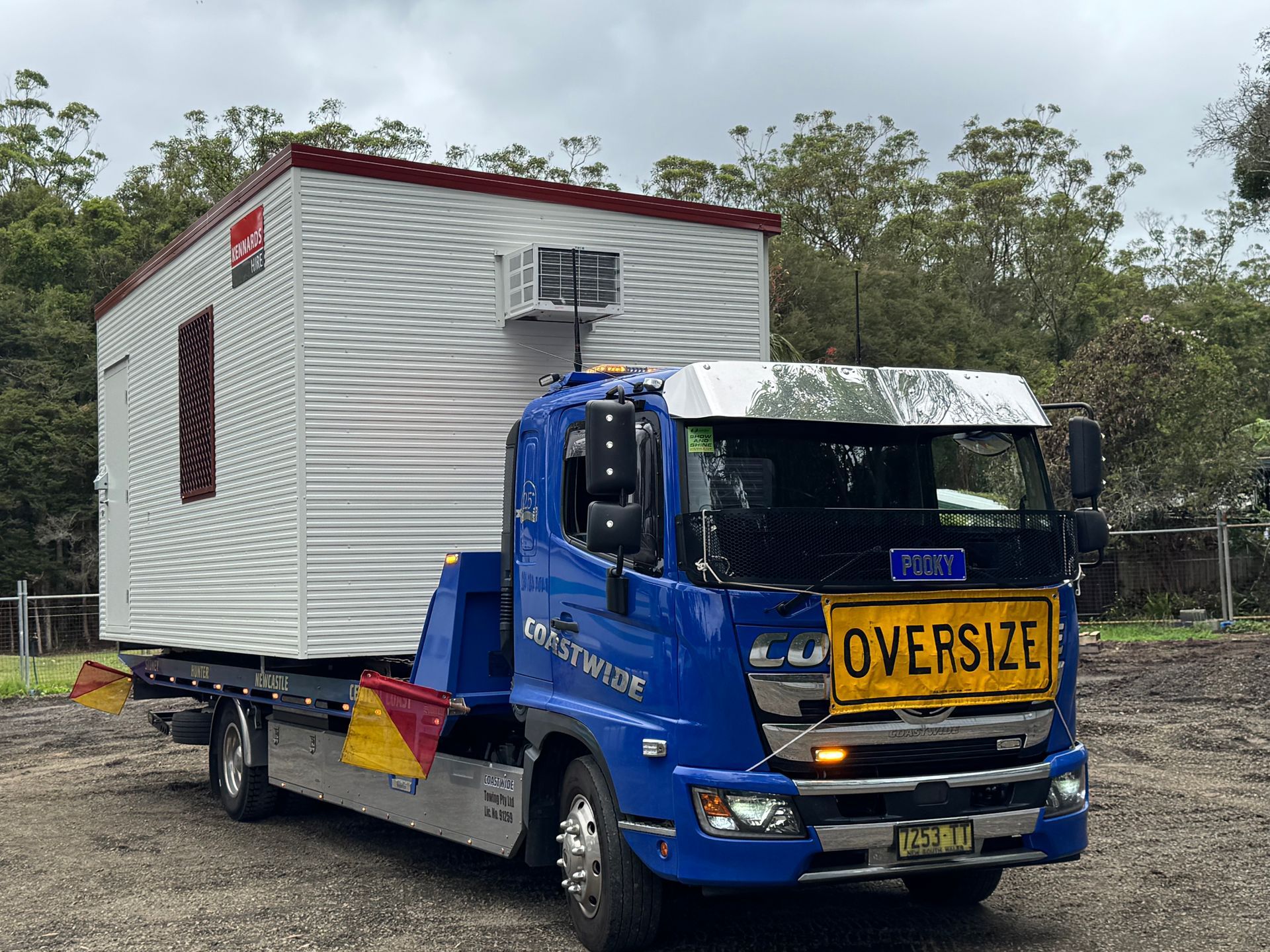 Blue truck carrying an oversized white portable building with a red roof, under an overcast sky. — Coastwide Towing & Transport In Berkeley Vale, NSW