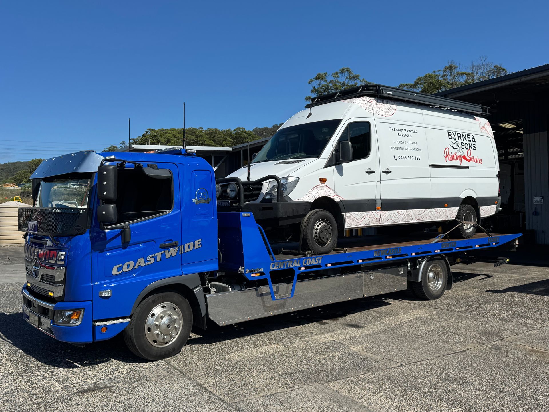 Blue tow truck carrying a white van, parked outside a building on a sunny day. — Coastwide Towing & Transport In Berkeley Vale, NSW