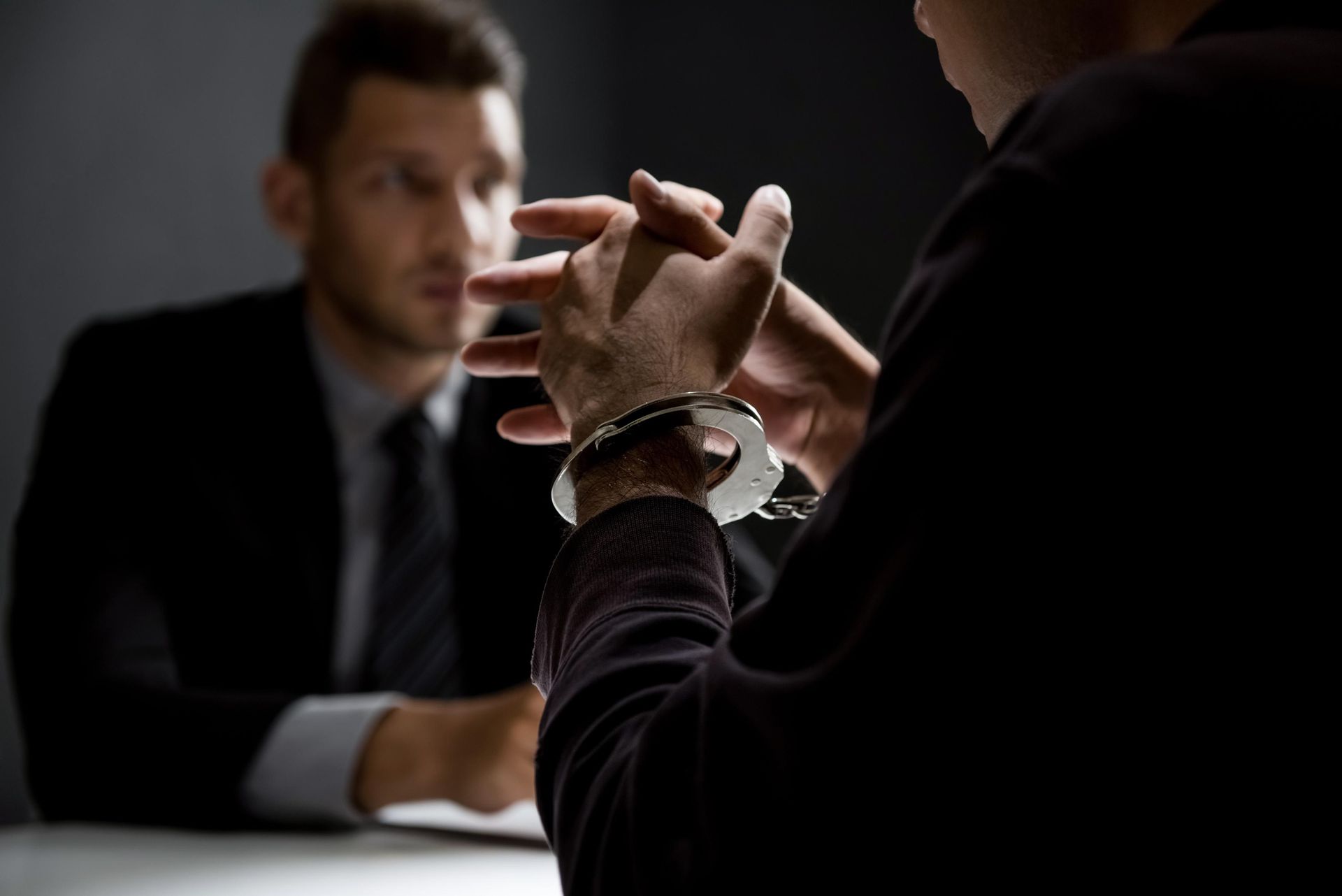 A man in handcuffs is sitting at a table talking to a man in a suit.