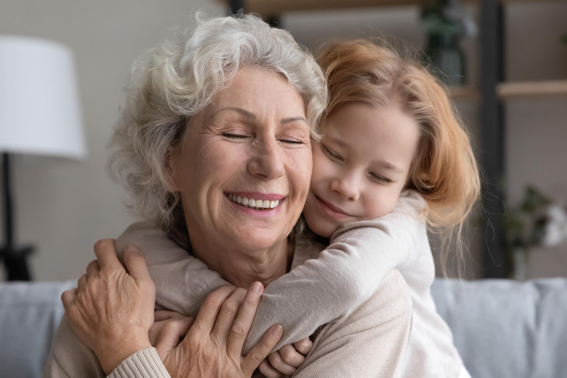 An elderly woman is hugging a little girl on a couch.