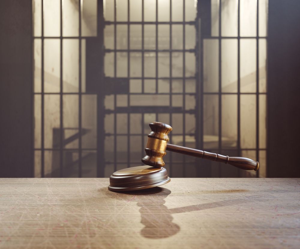 A wooden gavel in front of a jail cell.