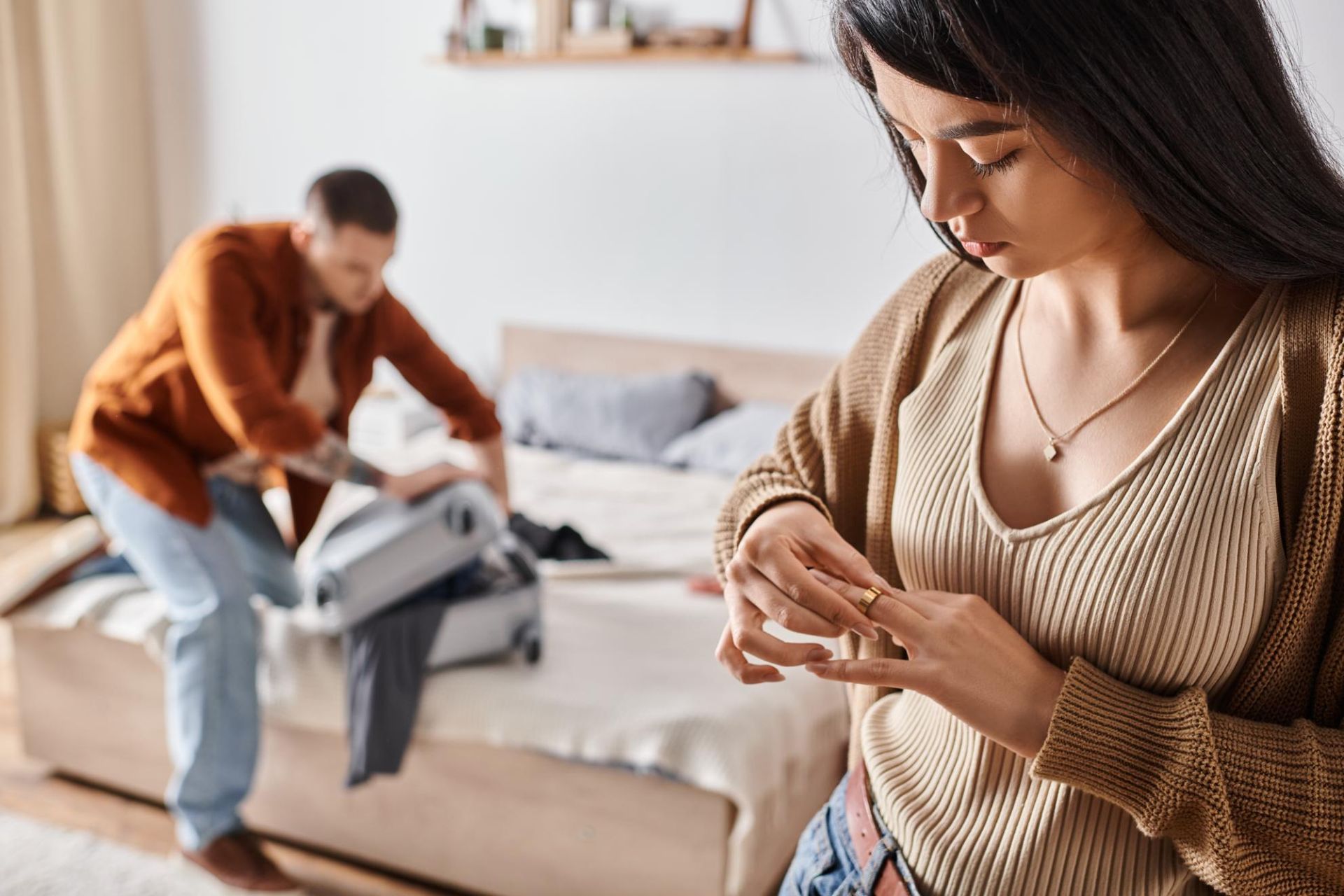 A woman is looking at her wedding ring while a man is packing a suitcase.
