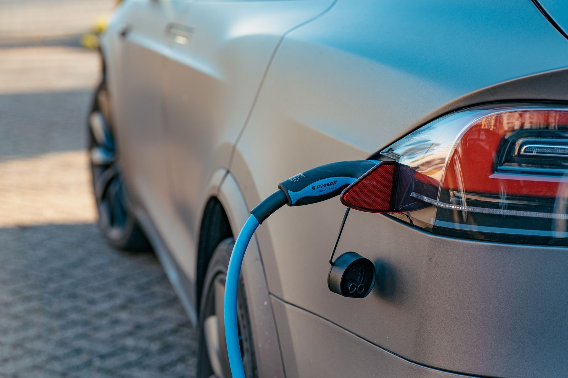 Electric car, light grey, charging with blue cable.