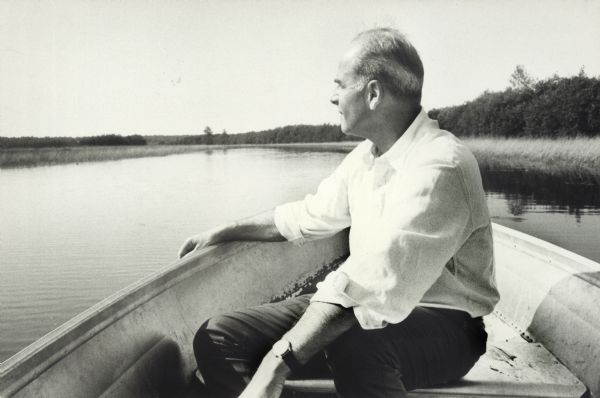 Man in a boat on a calm lake, looking toward the horizon.