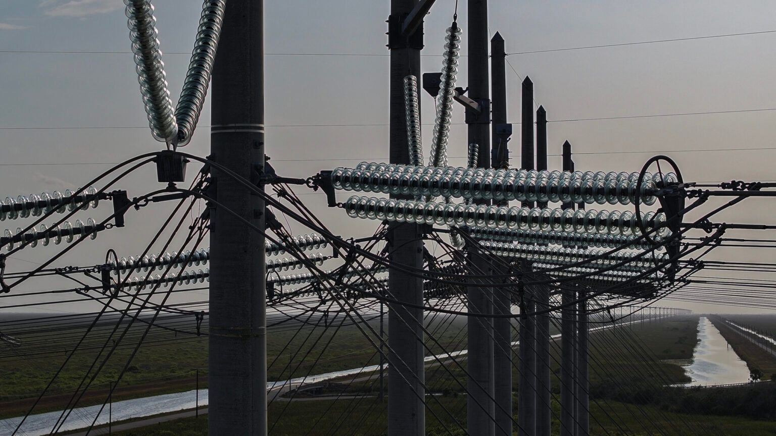 Rows of power line towers with insulators and wires in a rural landscape with canals.