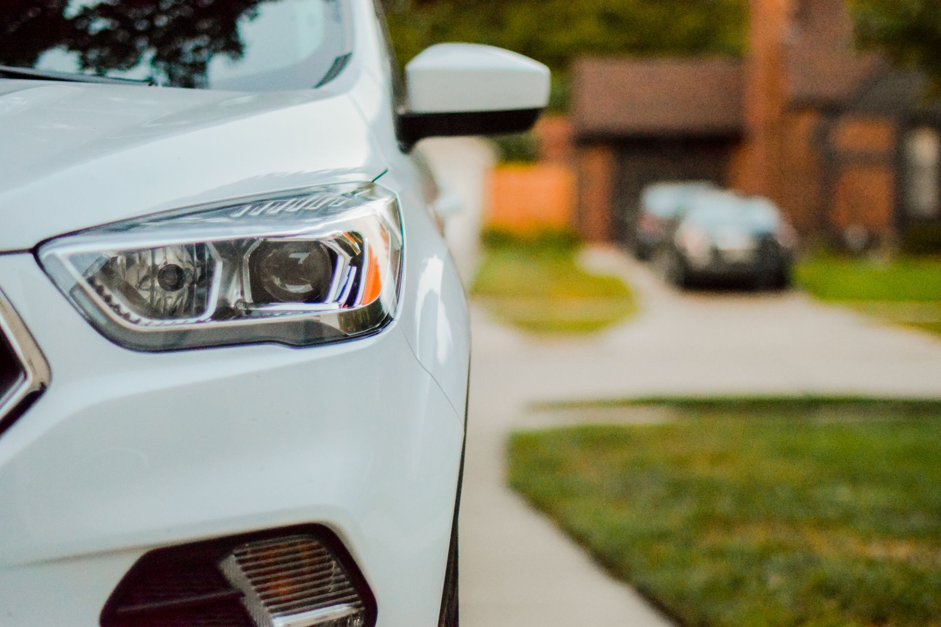 White car parked on a driveway in front of a house, with another car further back.