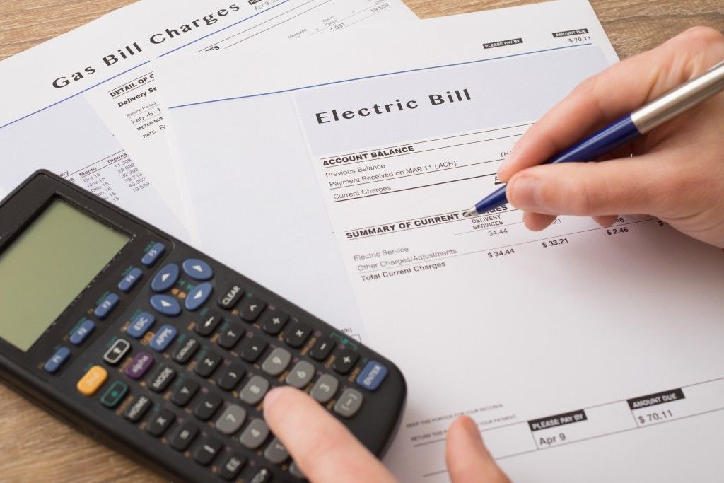 Person using a calculator and pen to review utility bills: electric and gas.