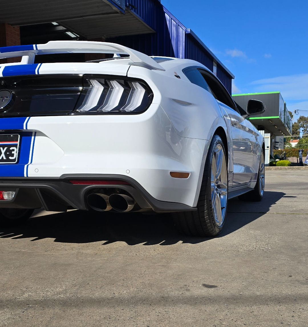 Close-Up of A Gray Car’s Twin Exhaust Pipes Above Wet Pavement and Grass — Bay City A1 Tyres in North Geelong, VIC